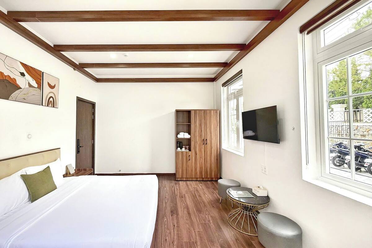 A bedroom with a bed, wooden wardrobe, TV, and a window with a view of parked motorcycles.