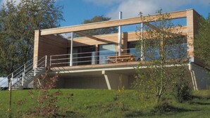 A modern house with a wooden deck, a staircase, and a large window overlooking a grassy area. - Exklusives Ferienhaus mit Terrasse und Garten by Interhome (Simmerath)