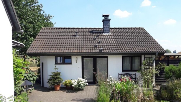Ein eingeschossiges Haus mit Ziegeldach, einer Haustür und einem kleinen Garten mit Teich.