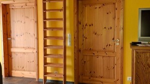 Ein Zimmer mit zwei Holztüren, einer Holzleiter, einem Fernseher auf einem Holzkasten und einem Fliesenboden.