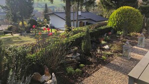 Una casa con techo de tejas, rodeada por un jardín con diversas plantas y flores.