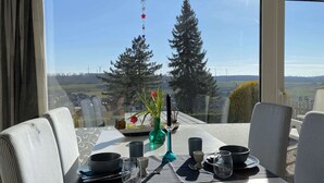 Mesa de comedor para dos personas, con vista a árboles y aerogeneradores al fondo.