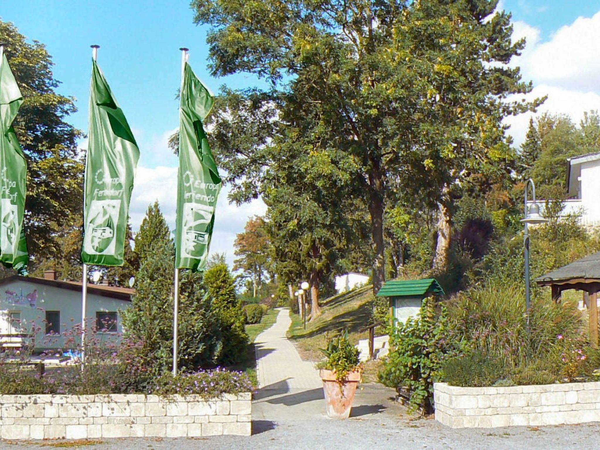 A pathway leading to a building with a green roof, surrounded by greenery and flags.