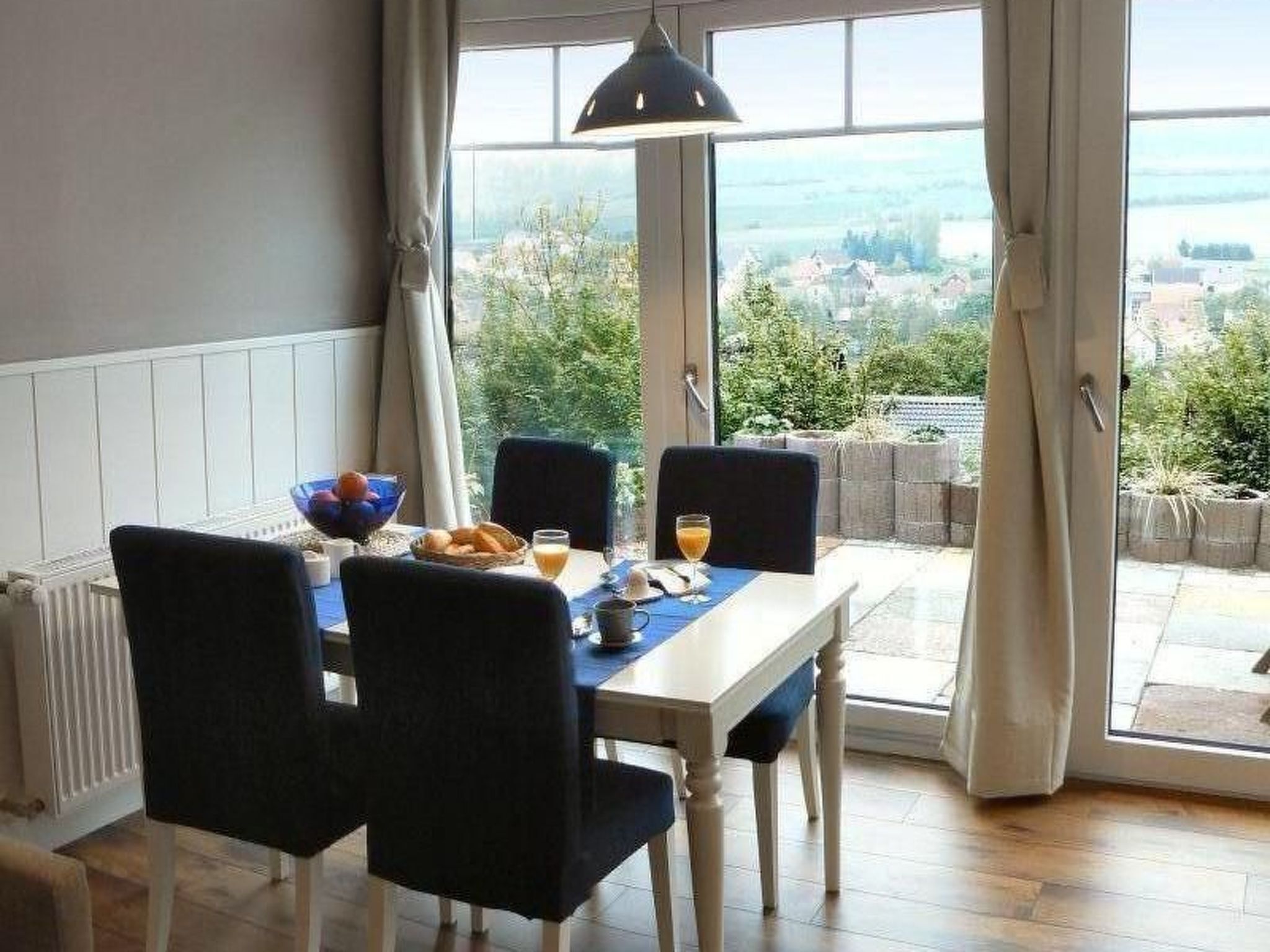 A dining area with a table set for two, a bowl of fruit, and a glass of orange juice.