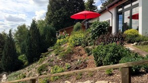 A wooden fence, a red umbrella, and a building with a stone retaining wall. - Belle Vue by Interhome (Husen)