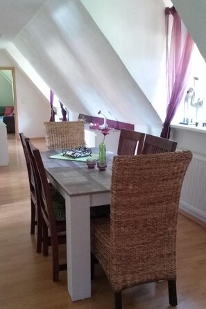 A dining area with a high ceiling and a sloped roof, featuring a wooden table and wicker chairs. - An der Königstrasse by Interhome (Tecklenburg)