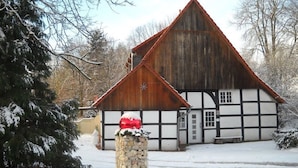A traditional half-timbered house with a steeply pitched roof, surrounded by snow-covered trees and a stone pillar with a red ornament. - An der Königstrasse by Interhome (Tecklenburg)