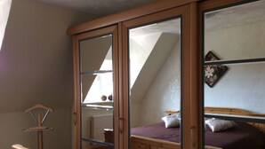 A bedroom with a sloped ceiling, wooden wardrobe with glass doors, a bed with a purple bedspread, and a radiator on the wall. - An der Königstrasse by Interhome (Tecklenburg)