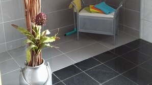 A small bathroom with a shower, a metal chair, a colorful towel rack, and a potted plant. - An der Königstrasse by Interhome (Tecklenburg)