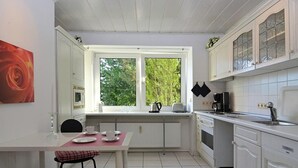 Moderni keittiö, jossa on valkoiset kaapit, ruokapöytä tuoleineen ja ikkuna, josta avautuu näkymä puita kohti.