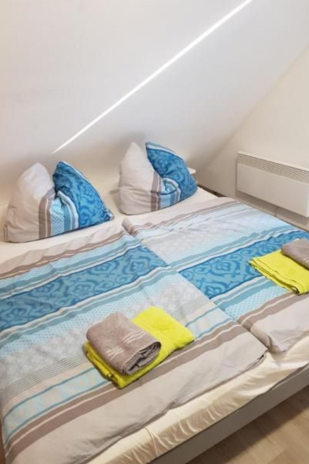 A twin room with two beds, each with patterned bedding and pillows, a white radiator, and a sloped ceiling.
