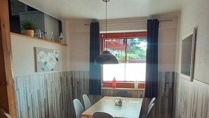 A dining area with a wooden table and chairs, a window with curtains, and a view of greenery outside. - Charmantes Ferienhaus mit Blick auf den Silberse by Interhome (Frielendorf)