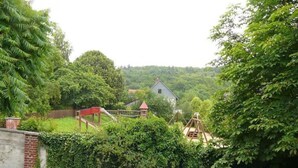 Landskab med legeplads, hus og frodig vegetation.