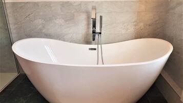 A freestanding bathtub in a bathroom with a tiled floor and a marble wall.