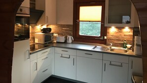 Une cuisine compacte avec des meubles blancs, un four à micro-ondes, un grille-pain et une fenêtre équipée de stores.