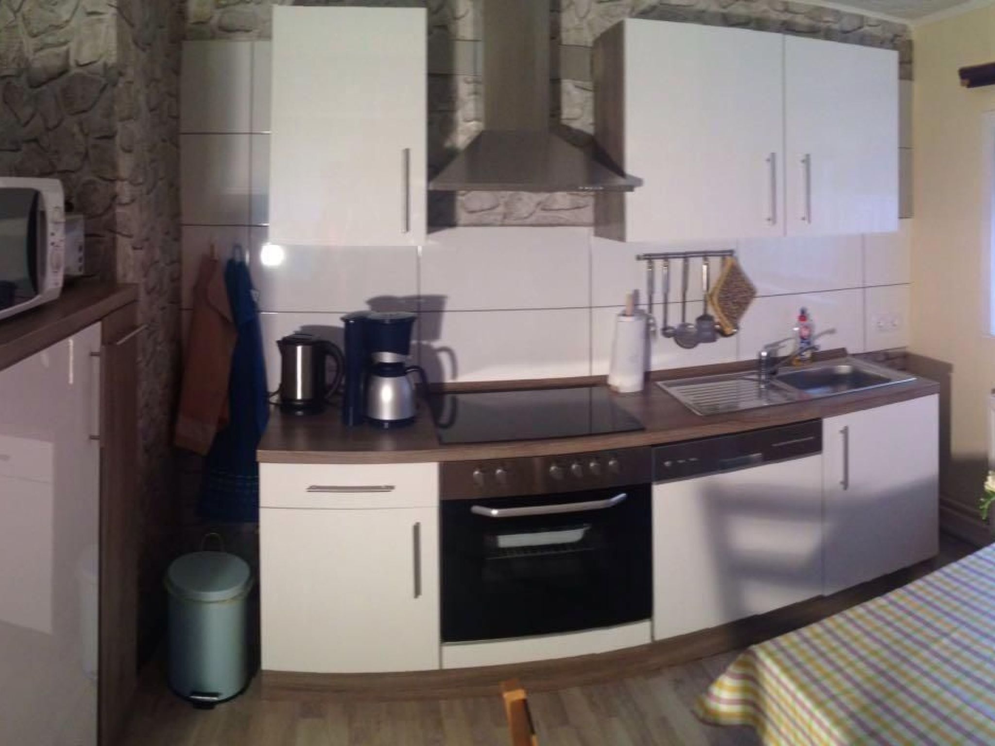 Una cocina compacta con gabinetes blancos, horno integrado, cafetera y lavamanos.