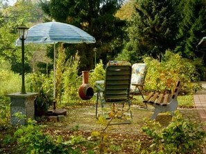 Un patio jardín con una sombrilla azul, un farol de piedra, una silla rústica y un banco de madera.