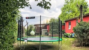 A trampoline with a safety net, surrounded by greenery and a red building in the background. - mit Terrasse by Interhome (Blankenburg)