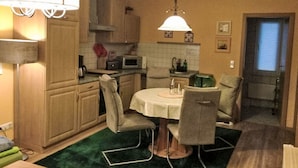 A compact kitchen with wooden cabinets, a microwave, a dining table with chairs, and a green rug. - mit Terrasse by Interhome (Blankenburg)