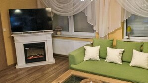 A living room with a green sofa, white cushions, a flat-screen TV on a fireplace mantel, and a glass coffee table. - mit Terrasse by Interhome (Blankenburg)