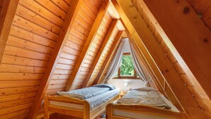 Un dormitorio de buhardilla con dos literas, una ventana con cortinas y vistas a la vegetación.