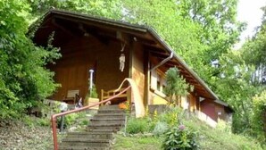 Una cabaña de madera con techo inclinado, una escalera que lleva a la entrada y un pequeño porche.