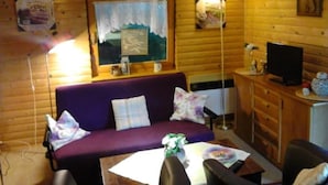 Un interior de cabaña acogedor, con un sofá morado, una mesa de comedor con un florero y un televisor sobre un mueble de madera.