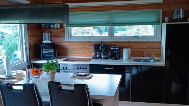 A modern kitchen with a central island, black bar stools, and a dining table. - Dachsbau by Interhome (Winsen / Aller)
