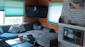 A cozy living room with a wooden ceiling, a stone fireplace, a flat-screen TV, and a comfortable seating area. - Dachsbau by Interhome (Winsen / Aller)