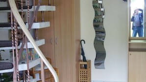 Een wenteltrap met houten afwerking, een vloermat met ruitpatroon, een houten kast en een wandspiegel.