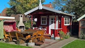 Een rode houten cottage met een schoorsteen, een houten tafel en een tuin.