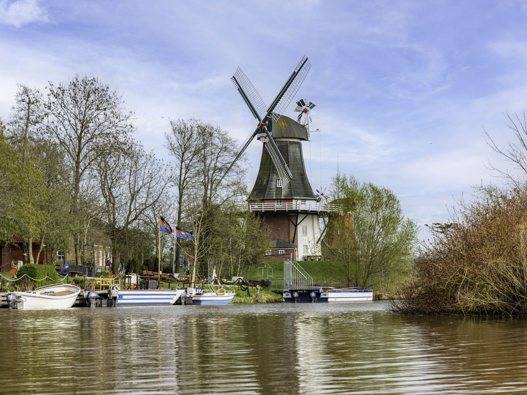 A traditional windmill by a calm river with boats docked nearby.