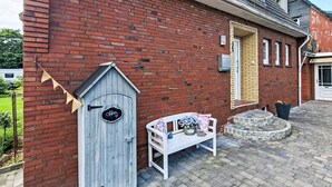 A brick building with a wooden door, a bench with flowers, and a small garden area. - Apartment Marion by Interhome (Greetsiel)