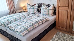 A bed with a plaid bedspread and pillows, a nightstand with a lamp, a wooden wardrobe, and a patterned rug. - Apartment Marion by Interhome (Greetsiel)