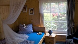 Ein Schlafzimmer mit Bett, Nachttisch, Lampe, einem Fenster mit Vorhängen und einem Bild an der Wand.
