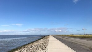A coastal road with a concrete sidewalk alongside a sandy beach. - in Sehestedt mit Garten by Interhome (Jade)