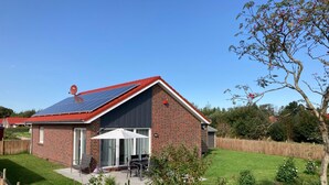 A house with a red roof, solar panels, a brick exterior, a patio with a table and chairs, and a well-maintained lawn. - in Sehestedt mit Garten by Interhome (Jade)