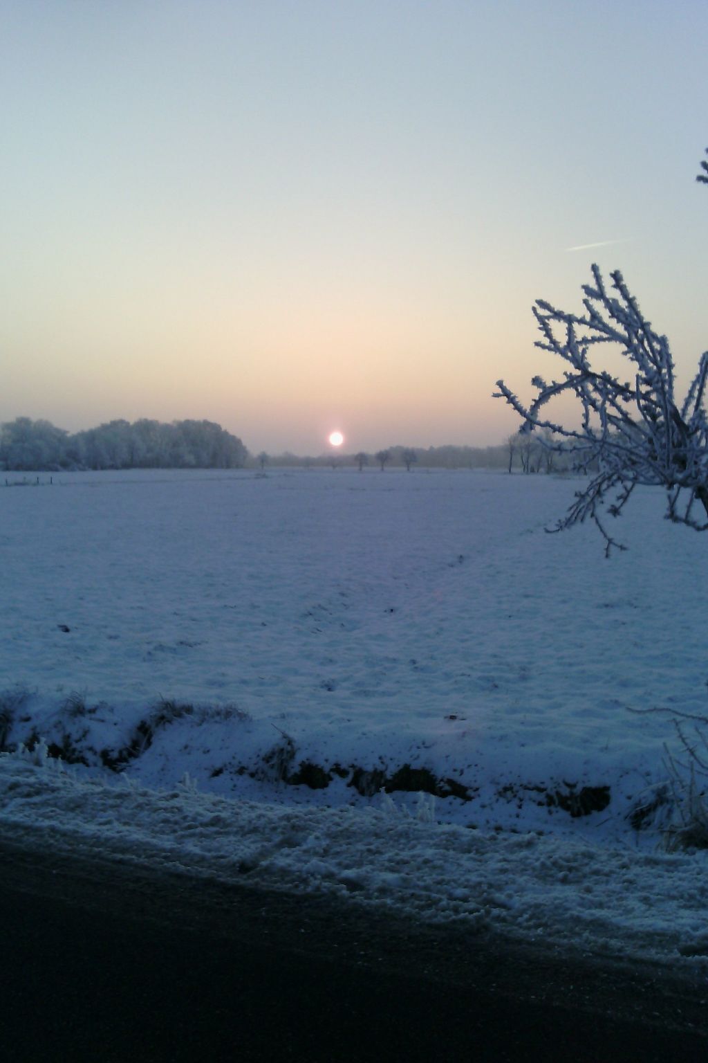 Schneebedeckte Landschaft mit klarem Himmel und untergehender oder aufgehender Sonne.