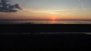 Auringonlasku rannalla, taivas on kirkas ja näkyvissä on lentokoneen jättämä kondenssijälki.