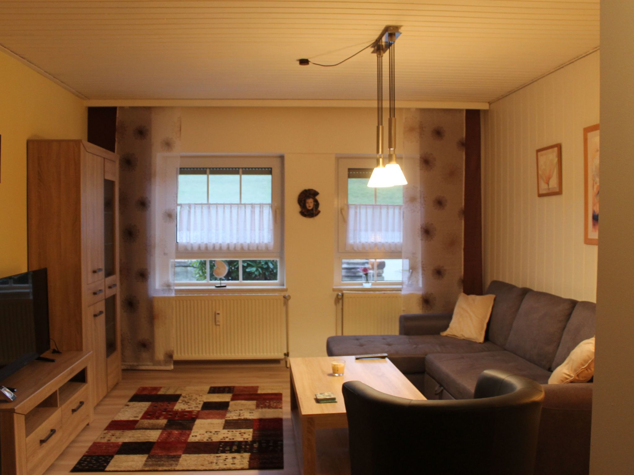En stue med sofa, sofabord, fjernsyn og et vindue med gardiner.