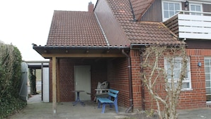 Ein zweistöckiges Haus mit Ziegeldach, Backsteinfassade und einer kleinen Veranda mit Tisch und Bank.