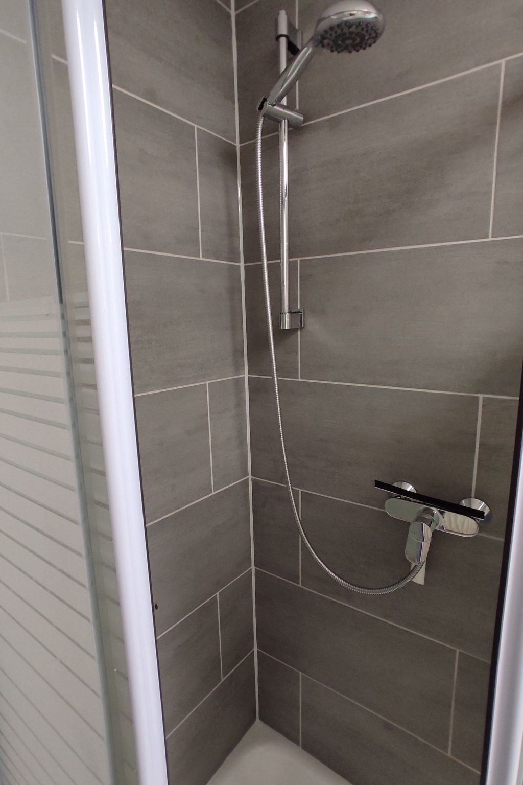 Eine Dusche mit Handbrause und Armaturen an der Wand.
