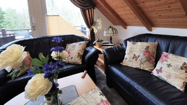 Un cuarto acogedor con dos sofás de cuero negro, cojines estampados, techo de madera y vistas al exterior con vegetación.