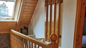 Una escalera de madera con barandilla, una ventana con vista a árboles y un farol en la baranda.