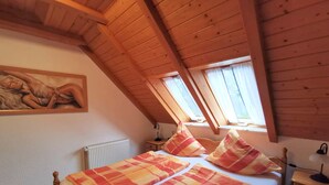 Un dormitorio con techo inclinado, vigas de madera, una cama con manta a cuadros, un radiador y un cuadro en la pared.