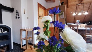 Un salón acogedor con chimenea, vigas de madera, una zona de comedor con mesa y sillas, y una cocina al fondo.