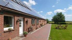 A brick building with solar panels on the roof, a paved walkway, and outdoor seating. - Landhaus Markus by Interhome (Süderschwei)