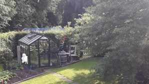 Een tuin met een glazen kas, een houten bankje en een pad.