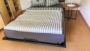 Een bed met gestreepte lakens, een klein nachtkastje met een lamp, en een houten kast.