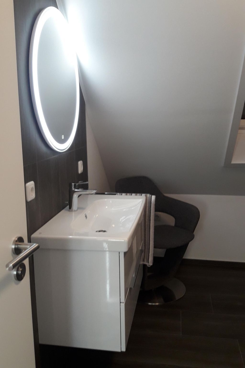 Un bany modern amb un rentamans blanc, un mirall amb il·luminació integrada i un sòl fosc.
